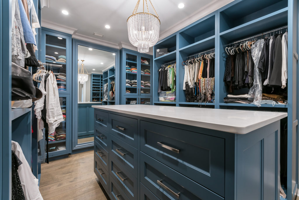 Blue painted master closet with open framed cabinet doors with glass panels. Closet Island features inset cabinetry with recessed panel doors and Emtek hardware. Long and short hanging.