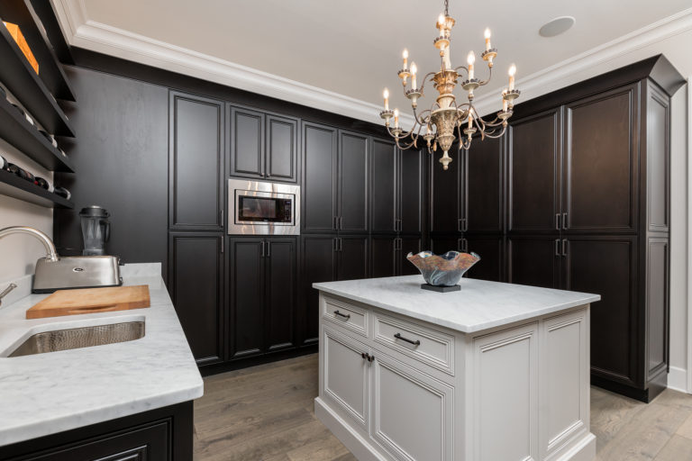 Custom built kitchen pantry featuring dark stained wood on inset cabinets with recessed doors. This pantry also features a white kitchen island with doors and drawers and all of the cabinetry is decorated with Top Knobs hardware